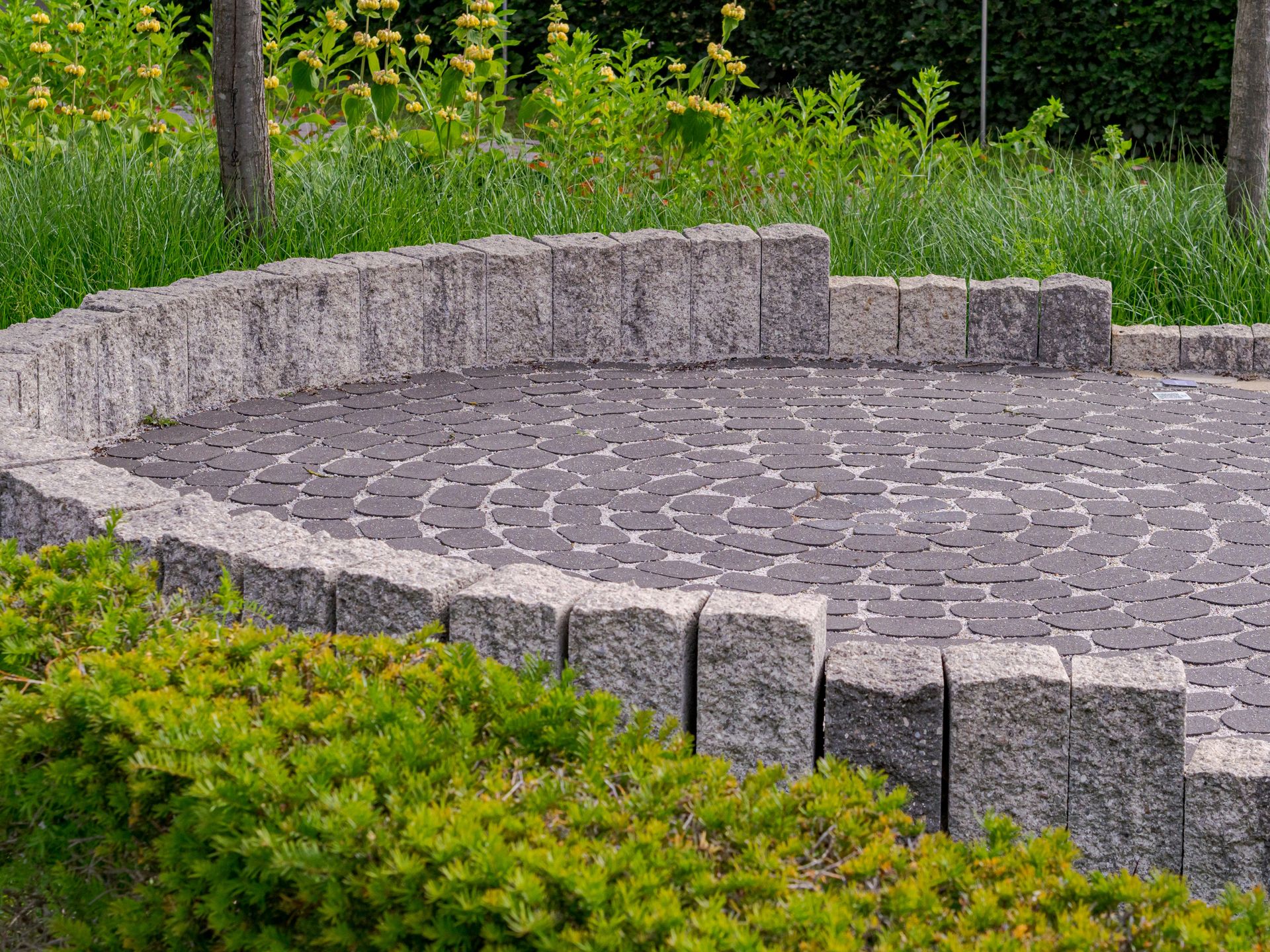 Circular paved patio with low stone wall and green bushes.